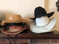 Photo of six hats stacked on a wooden surface including straw and felt cowboy hats