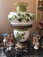 Front view of vintage floral painted glass lamp with brass fittings and green frosted ruffled shade, showing detailed leaf and flower pattern.