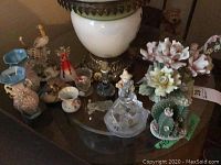Overall table view showing various porcelain and ceramic figurines, vase, and floral decorations under a lamp.