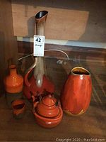 Photo showing all items in the lot: four orange pottery vases of varied sizes and an orange enamel kettle, placed on a wooden surface