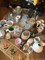 Wide view showing the assortment of mugs, glasses, ceramic kitchenware, and decorative items on a table and floor
