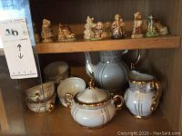 Shelf displaying Japanese white and gold-trimmed tea set including teapot, sugar bowl, creamer, cups and saucers next to Wade figurines.