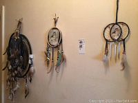 Photo of six dream catchers hanging on wall, showcasing variety of sizes, designs, feathers, and beads