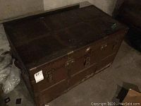 Full view of the vintage metal trunk showing wear and rust on its surface.