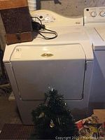 White Maytag Neptune dryer with its front and top visible. Control panel shows dry temperature and option buttons.