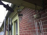 Outdoor photo of multiple wind chimes hanging on porch with metal tubes and a wooden top