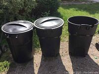 Photo showing three black Rubbermaid garbage bins side by side outdoors, two with lids, one without.