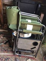 Stacked folding chairs showing Mountain Ridge green fabric directors chairs with product tags and attached side tables