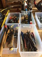 Multiple hand tools including hammers, pliers, socket set pieces in plastic containers on a wooden surface