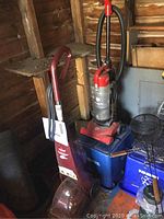 Photo showing Bissell QuickSteamer Power Brush in burgundy color with power cord wrapped on handle, upright against wooden wall.