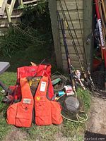 Overview of fishing equipment including life jackets, fishing rods with reels and fishing nets on grass