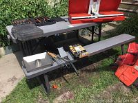 Full view of the picnic table with attached benches on grass and concrete patio, showing included grilling utensils and cases on the table.