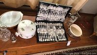 Overview of lot items on table including flatware case open, Pyrex casserole, decanter, serving bowl, platter underneath