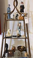Overall photo showing shelf unit with various knickknacks including figurines, an owl coin bank, multicultural souvenirs mostly figurines, and damaged item identified by seller