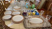 Overview of china plates, crystal glasses, coffee sugar and creamer set, colorful cups and saucers, serving trays on table