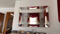 Wide view of the large rectangular beveled glass wall mirror mounted on the wall, showing surrounding room and red curtains.
