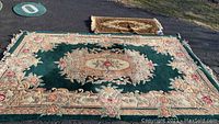 Photo showing the large green wool rug and smaller beige wool throw rug side by side laid out on pavement