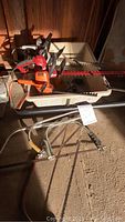 Photo showing two electric hedge trimmers resting on a plastic cart inside a garage. Floor is concrete and lighting is dim with some sunlight.