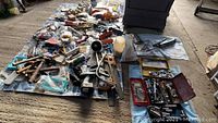 Wide view of assorted home repair and workshop items spread out on blue tarps and mats, including hand tools, power tools, hardware, and gadgets.