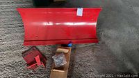 Plow attachment laid on the ground showing full red metal blade with mounting areas.
