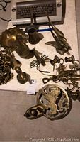 Overview of various brass items including dolphin figurine, brass lobster, hardware, and trivet beside a keyboard
