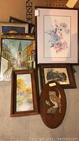 Grouped wall art, various framed paintings and decorative wooden plaque, varying sizes and styles visible