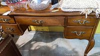 Full view of the desk showing top surface with items and front drawers and brass handles.