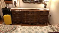 Front view of the dresser showing nine drawers, polished wood surface with decorative edge, and part of a rug on the floor.