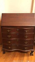 Front view of the closed secretary desk showing dark wood finish, drop front panel, lock, and brass handles on drawers.