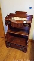 Front view of the vintage night stand showing the top decorative back, two small side drawers, a rounded front drawer below, open shelving, and the large bottom drawer with metal handles.