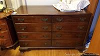Front view of the vintage wooden dresser showing 8 drawers with brass handles and curved feet on wooden floor.