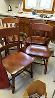 Four vintage Heywood Wakefield wooden dining chairs grouped together showing wood finish wear and scuffs