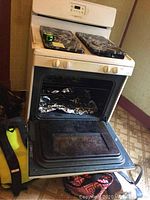 Full view of white gas stove with four burners and oven. Oven door is open with foil inside.