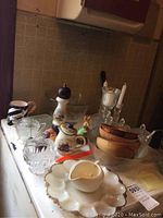 Overview of kitchenware on countertop including ceramic dishes, wooden bowls, glass candle sticks, gravy boat, and decorative items.