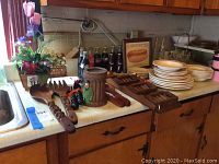 Overview of kitchen countertop with large wooden decorative fork and spoon, ceramic plates, collectible Coke glass bottles, and other kitchen items.