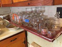 Photo of multiple Christmas-themed glasses and mugs on a wall shelf alongside a frosted glass tree decorative piece.