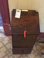 Front view of dark wood vegetable bin with top lid closed showing carved 'taters n onions' text and orange pull tab.