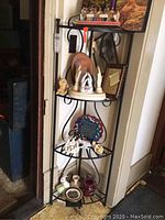 Black metal corner rack filled with various decorative items: figurines, photo frames, plates, and small collectibles, seen from front angle.