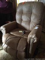 Full view of the tan brown Catnapper electric lift recliner chair showing its padded back, seat, and armrests with remote control on the seat.
