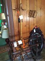 Full view of the tall wooden coat rack with multiple hooks and part of the wooden quilt rack in front of a wood-paneled wall.
