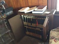 Wooden cabinet open showing shelves filled with encyclopedia volumes and additional books on top