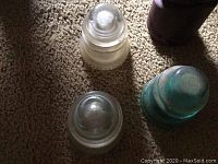 Three vintage glass electrical insulators in clear and blue-green colors, viewed from above on carpet.