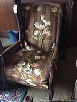 Front view of wingback chair showing the floral upholstery and wooden armrests.