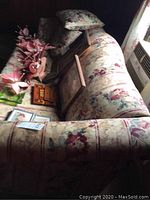 Photo of sofa with floral upholstery, showing the long side with cushions removed and various picture frames resting on it.