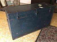 Full front view of large vintage wooden and metal trunk with latches and metal corner reinforcements.