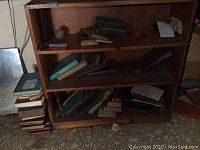 Front view of wooden bookshelf with books on shelves and stacked next to it on floor