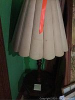 Lamp with beige scalloped lampshade, wooden base, and a visible orange ribbon attached to the shade.