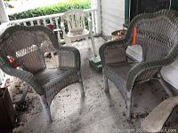Two faux wicker chairs on a porch, light gray painted finish with visible dirt on the seats and floor around.
