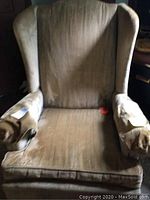Front view of upholstered wing chair showing fabric texture, wing design, armrests, and overall condition with discoloration and wear.