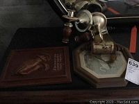 Photo showing two silver-toned metal candle sconces with wooden elements, laid on a table with a plaque beside them